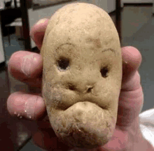 a potato with a face carved into it is being held in a person 's hand .