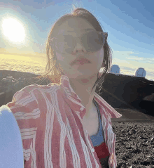 a woman wearing sunglasses and a striped shirt is taking a selfie on a mountain .