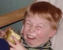 a young boy with red hair is making a funny face while holding a banana .