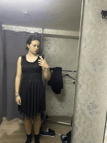 a woman is taking a selfie in a dressing room in a black dress .