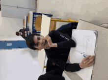 a boy wearing a black shirt that says " keep your " sits at a desk in a classroom