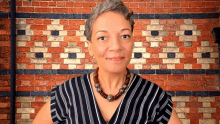 a woman wearing a striped shirt and a necklace is standing in front of a brick wall