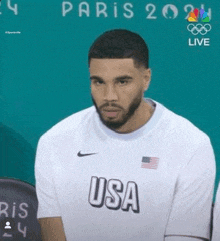 a man with a beard is wearing a usa t-shirt and sitting in a chair .