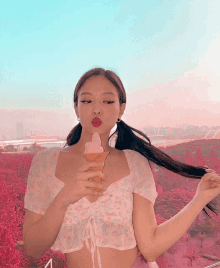 a woman in a pink top is holding an ice cream cone and blowing a kiss