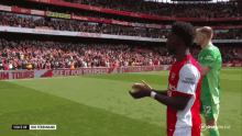 a soccer player in a red and white jersey stands in front of a banner that says emirates stadium tours