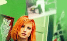 a woman with red hair is standing in front of a green wall looking at something .