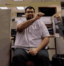 a man in a plaid shirt sits in a cubicle in front of a sign that says ' a '