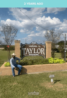 a man in a cowboy hat is sitting in front of a sign that says welcome to taylor