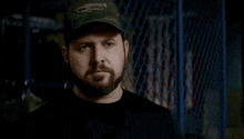 a man with a beard wearing a hat and a black shirt is standing in front of a locker .