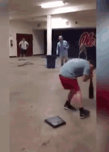 a man in a blue shirt and red shorts is squatting down in a room with a coca cola sign on the wall