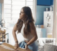 a woman in a white crop top and blue shorts is standing at a table .