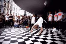 a man doing a handstand on a checkered floor in front of a crowd wearing a t-shirt that says wow