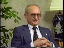 a man in a suit and tie is smiling while sitting in front of a lamp .