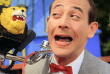 a man in a suit and bow tie is talking into a microphone with a toy lion in the background