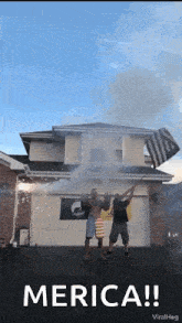 a group of men are standing in front of a house holding a flag and smoke coming out of it .