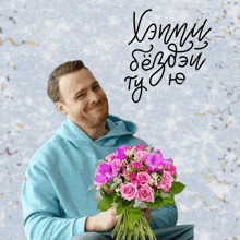 a man in a blue hoodie is holding a bouquet of pink flowers in front of a sign that says kommu