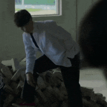 a man in a white shirt and tie is kneeling on a pile of bricks in front of a window