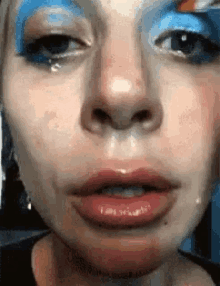 a close up of a woman 's face with blue and white makeup and a tear coming out of her eye .