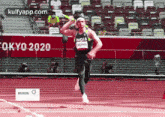 a man is running on a track in a stadium with a sign that says tokyo 2020 on it .