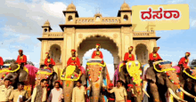 a group of people riding on the backs of elephants in front of a building with a sign in kannada