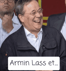 a man with glasses and a black jacket laughs with a sign that says armin lass et.