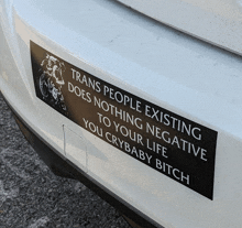 a white car has a bumper sticker that says trans people existing does nothing to your life you crybaby bitch