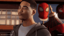 a man in a grey hoodie stands in front of a spiderman mask