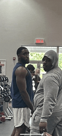 two men standing in a gym with a red exit sign on the wall