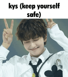 a young man in a white shirt and black tie giving a peace sign with the words kys ( keep yourself safe ) below him