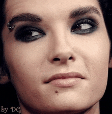 a close up of a man 's face with a piercing in his eyebrow and smokey eye makeup .