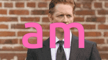 a man in a suit and tie stands in front of a brick wall with the word am written in pink