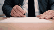 a man in a suit is writing on a piece of paper with a pen