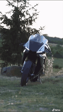 a motorcycle is parked in a grassy field with a tree in the background and a tiktok watermark