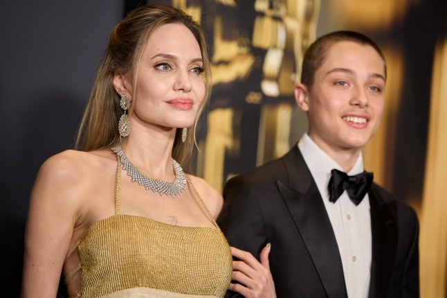 Angelina Jolie with son Knox Jolie-Pitt on the red carpet. Angelina wears a gold dress and large silver jewellery, while Knox wears a black tux, white shirt and black bow tie