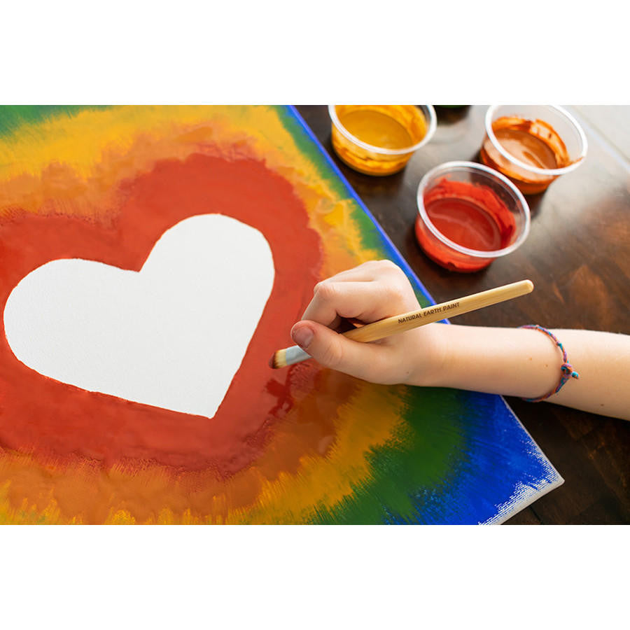 A child's hand painting a canvas with plastic cups of paint in the background