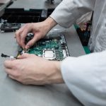 Close up of two hands working on an electronic component on an assembly line