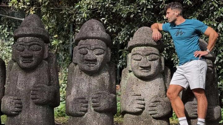 Stefan leaning on the hat of a stone statue next to two other identical stone statues.