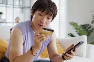 A young man uses his credit card online with his phone.