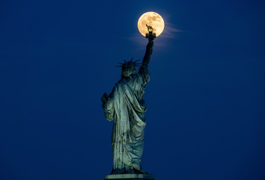 The Flower Moon rises behind the Statue of Liberty in New York City.