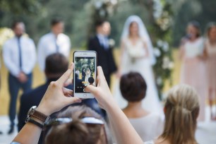 A guest at a wedding ceremony taking a picture of the bride and groom with their phone