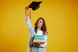 Graduate girl in a graduation hat on her head, with books stands