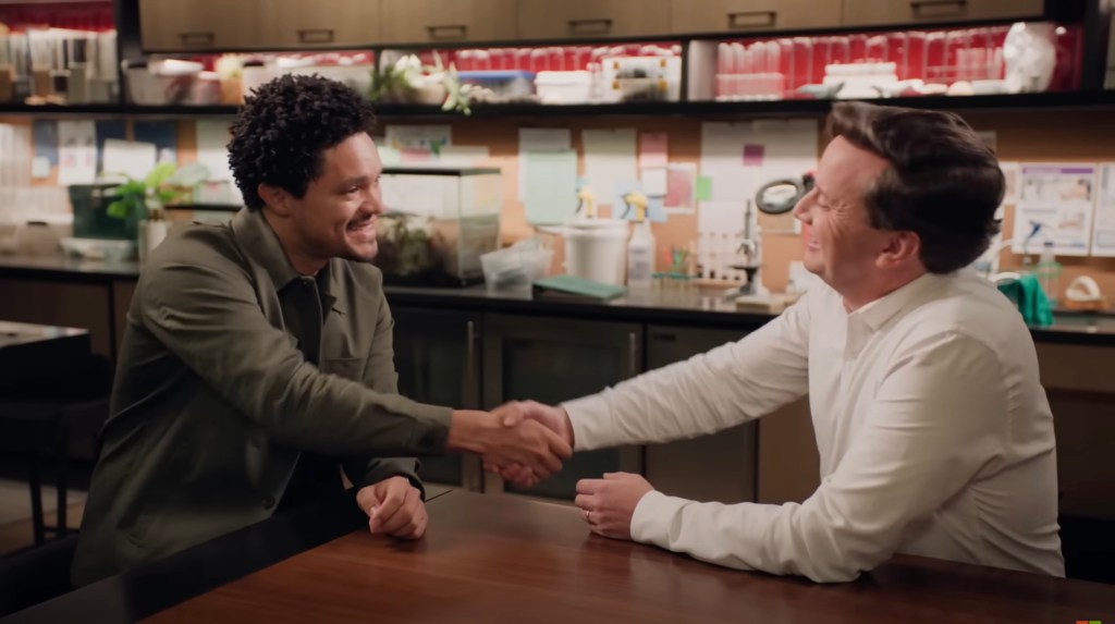 Trevor Noah shaking hands with another man, screenshot from video titled 'AI is sometimes the only solution | The Prompt with Trevor Noah'