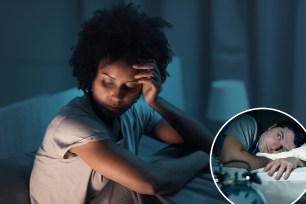 Stressed African American woman sitting in bed at night, unable to sleep and with her head in her hand