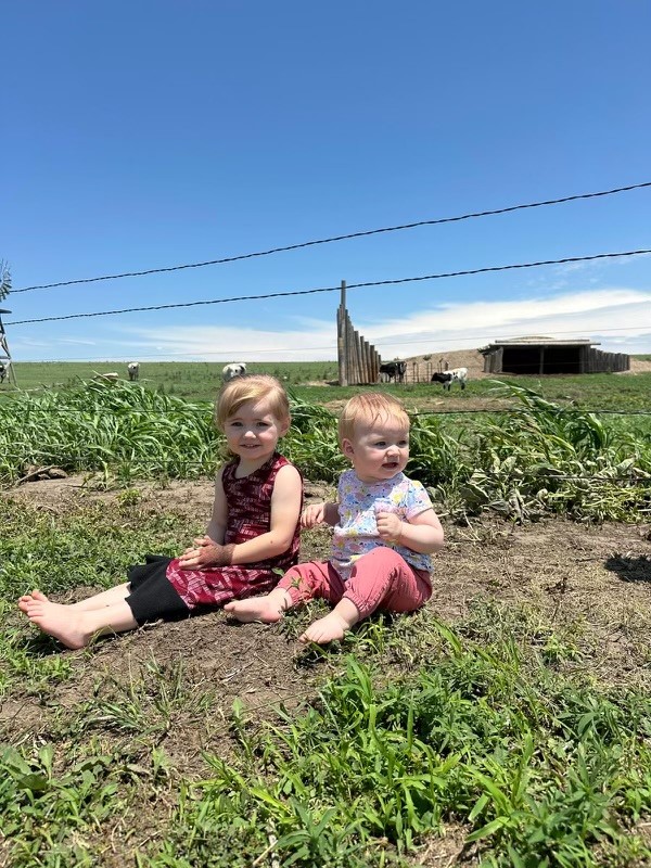 Two young children, Madilynn Grace and Haylie Faith Unger, sitting in the grass in rural Haskell County, Kansas