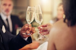 A pair of hands holding champagne glasses, representing the wealth associated with higher risk of cancer