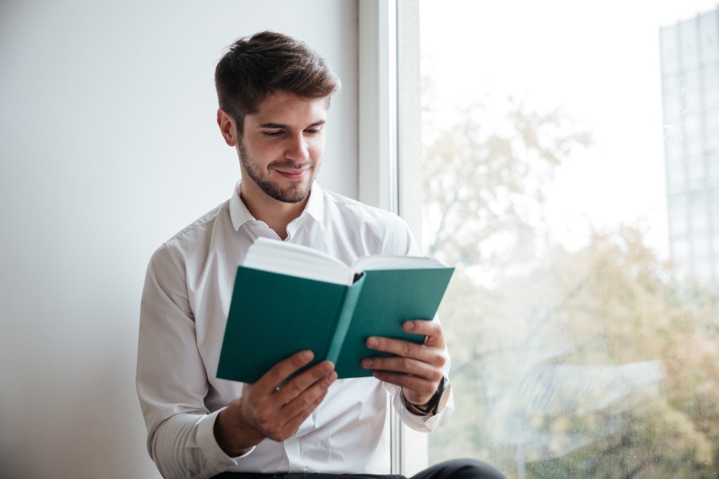 businessman dressed in white shirt sitting in cafe and reading a book