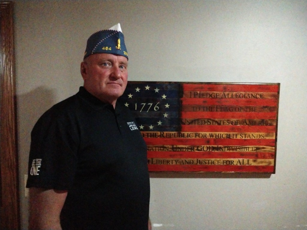 Tom Behrends standing in front of an American flag woodworking