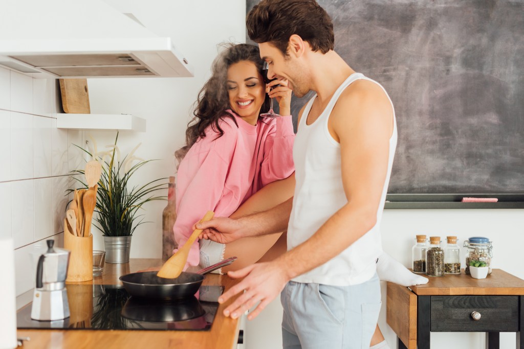 man cooking near woman holding glass of wine on kitchen worktop