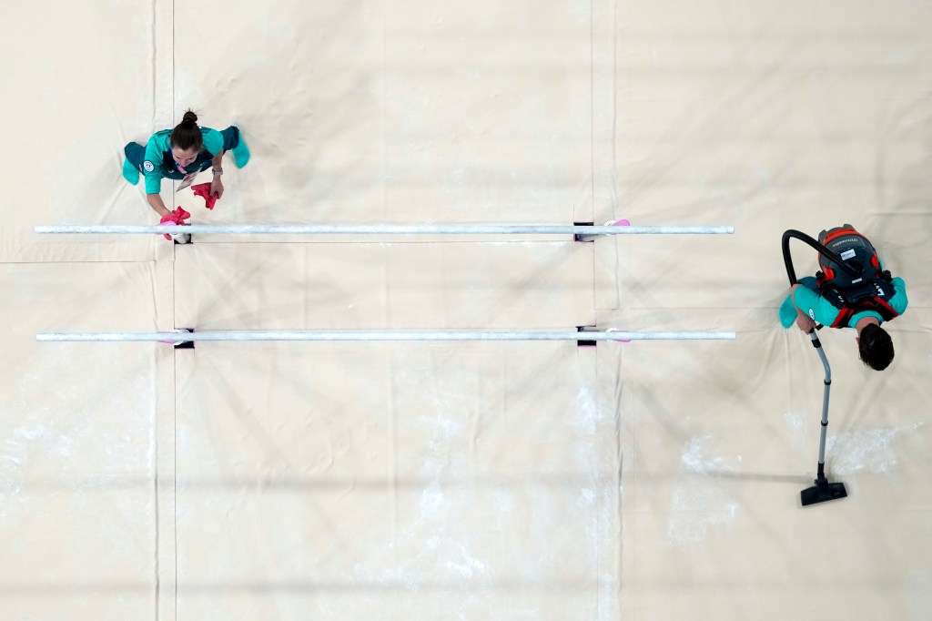 Workers cleaning the parallel bars after a men's gymnastics practice session at the 2024 Summer Olympics in Paris, France