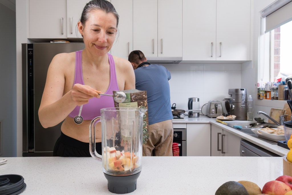 Middle-aged woman in fitness clothing making a detox smoothie in her kitchen